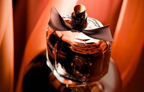 Perfume bottle with black bow, elegant design, luxury fragrance, warm lighting, reflective surface for high-end branding.